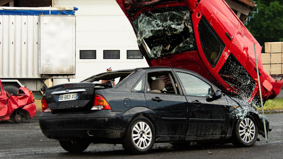A thrilling car stunt crash with a red car flipped onto a black vehicle in an outdoor setting.